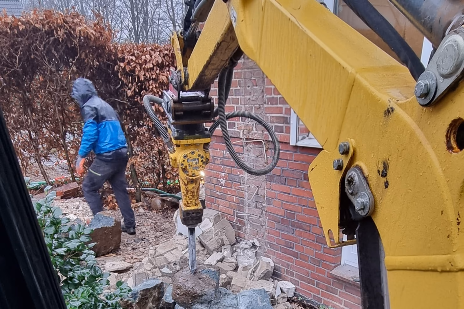 Abbrucharbeiten mit dem Hydraulikhammer am Bagger, ein Mitarbeiter räumt gelöstes Mauerwerk beiseite