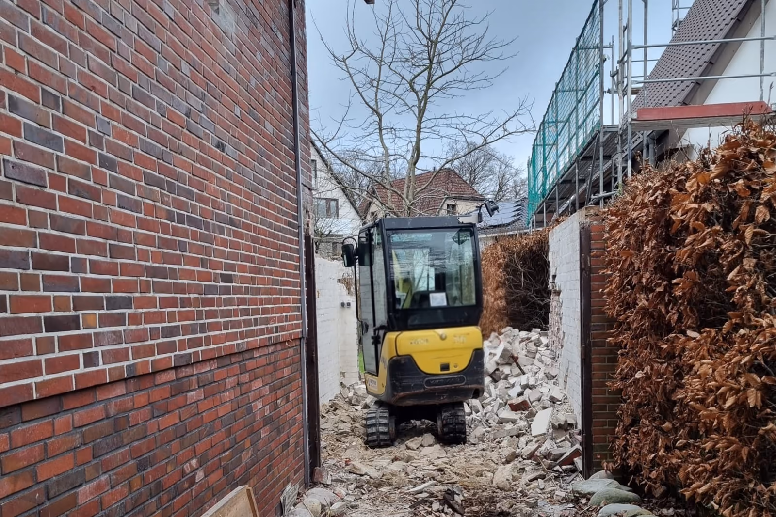 Minibagger arbeitet in der schmalen Gasse zwischen Hauswand und Grundstücksgrenze