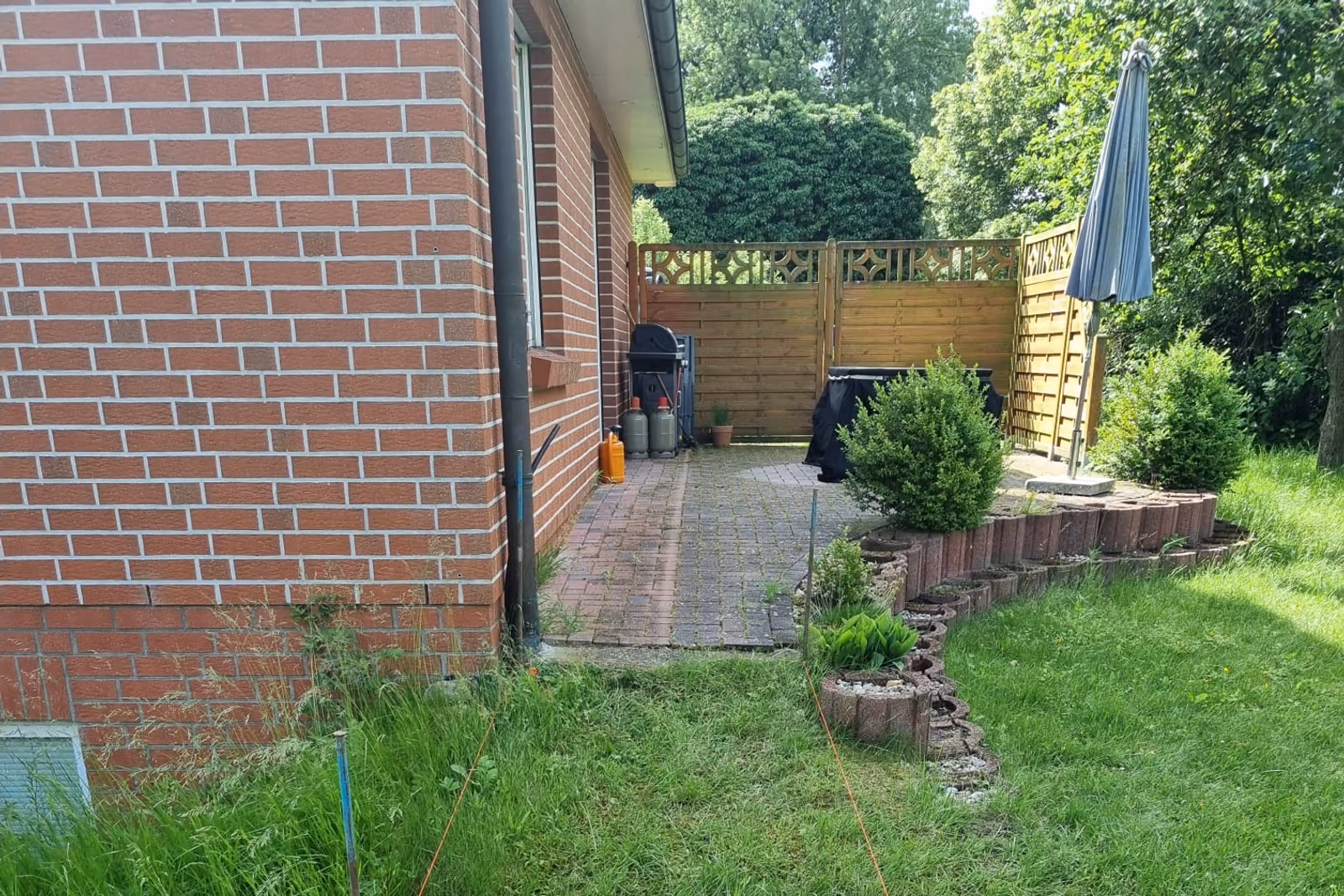 Beeteinfassung aus Natursteinen entlang eines gepflasterten Weges an der Hausecke